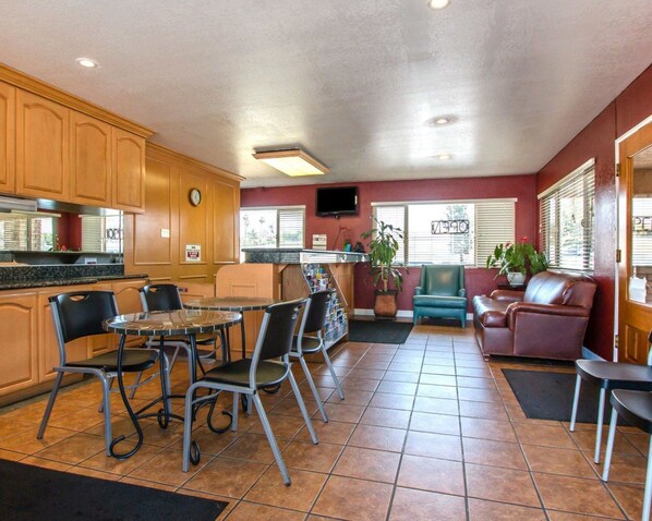 Une cuisine compacte avec des meubles en bois et un coin repas avec des chaises en métal. On y trouve également un petit coin salon avec un canapé et un téléviseur fixé au mur.