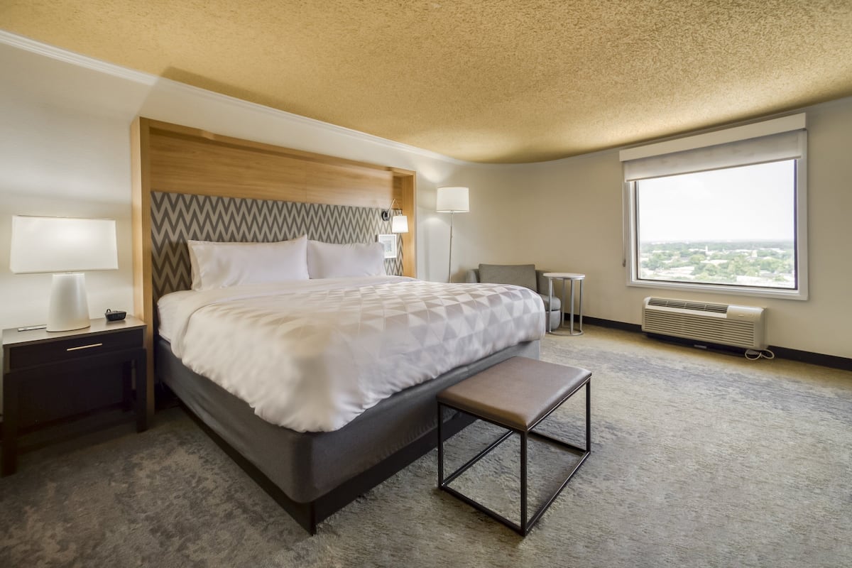 A hotel room with a large bed, bedside lamps, a bench, a desk, and a window with a view.