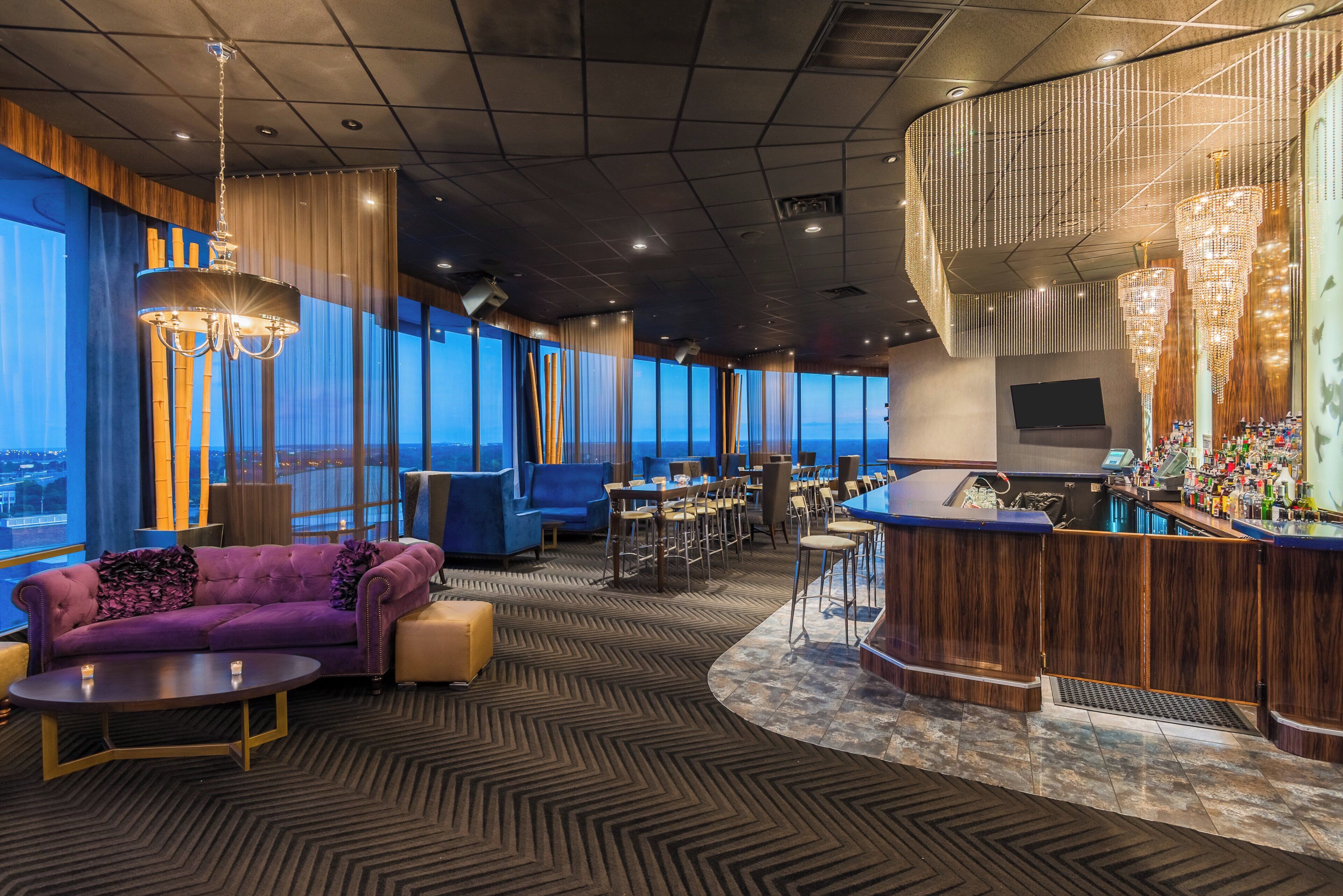 A modern lounge area with a bar, seating, and large windows offering a view.