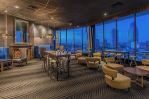 Un salon moderne doté d’une grande fenêtre donnant sur une vue panoramique de la ville au crépuscule.
