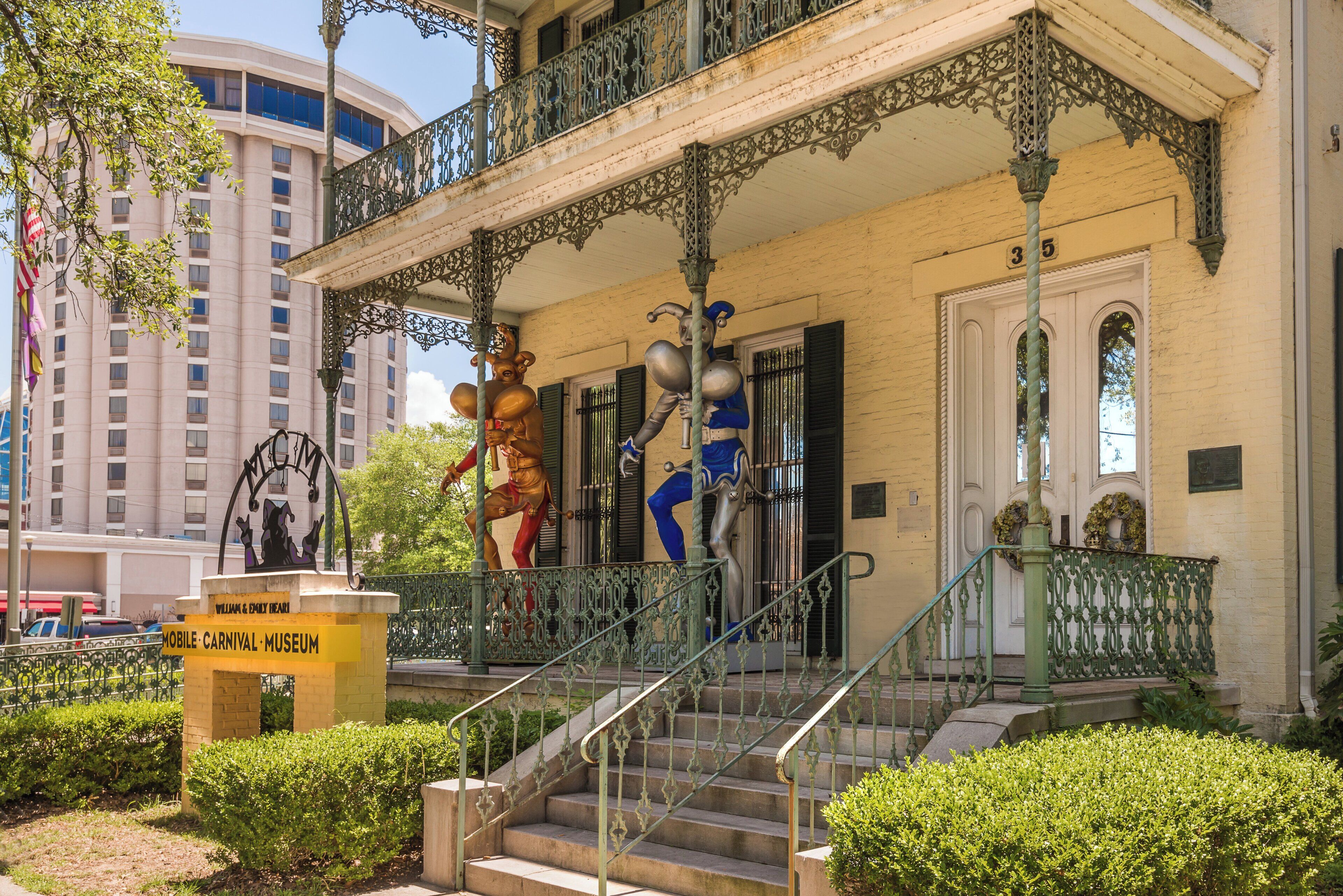 Um edifício com grades de ferro elaboradas, uma escadaria e uma estátua de uma pessoa vestida de vermelho.