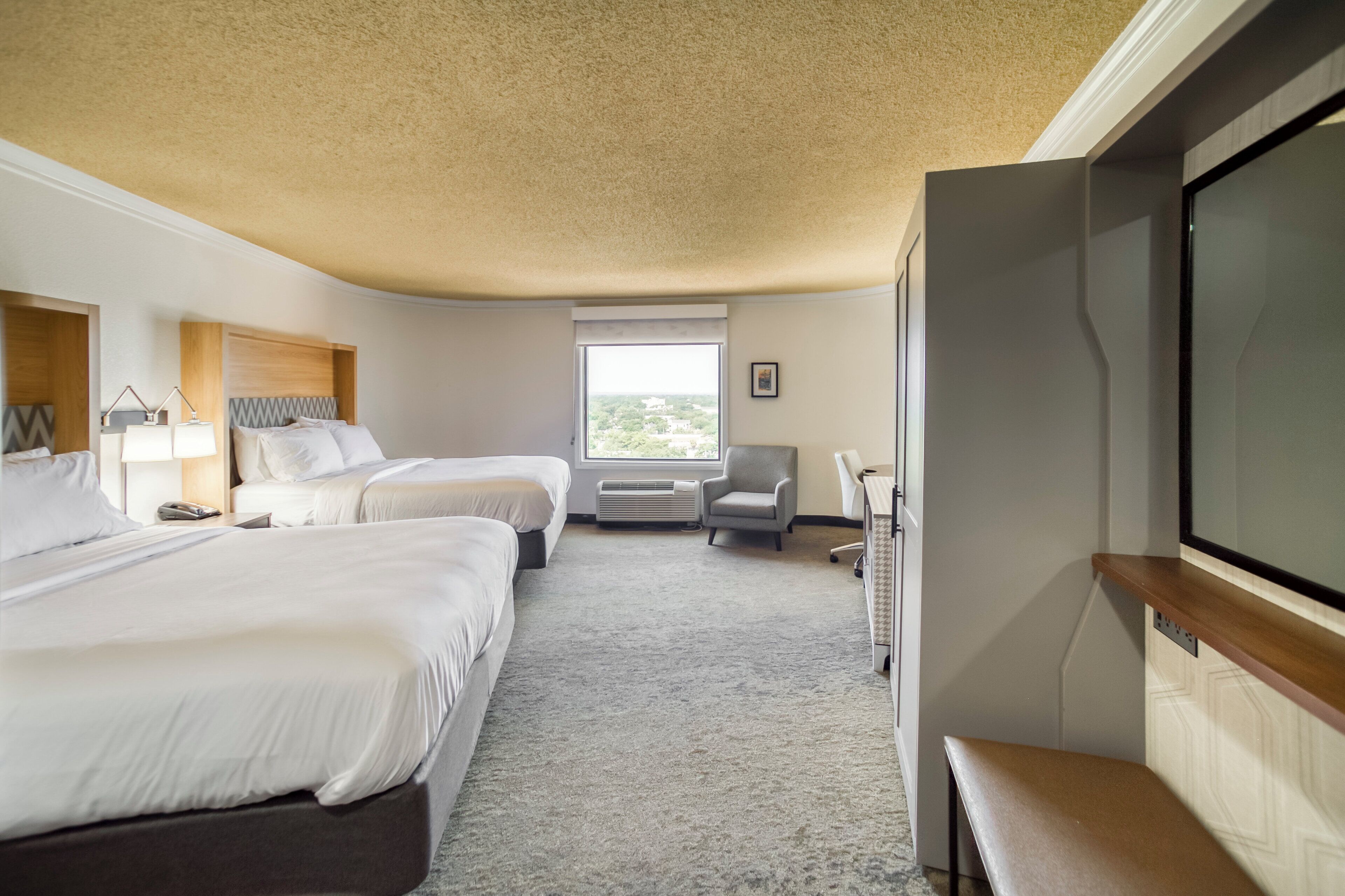 A hotel room with two beds, a desk, a chair, a television, and a window with a view.
