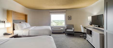 Een hotelkamer met twee bedden, een bureau met een computer, een televisie en een raam met uitzicht.