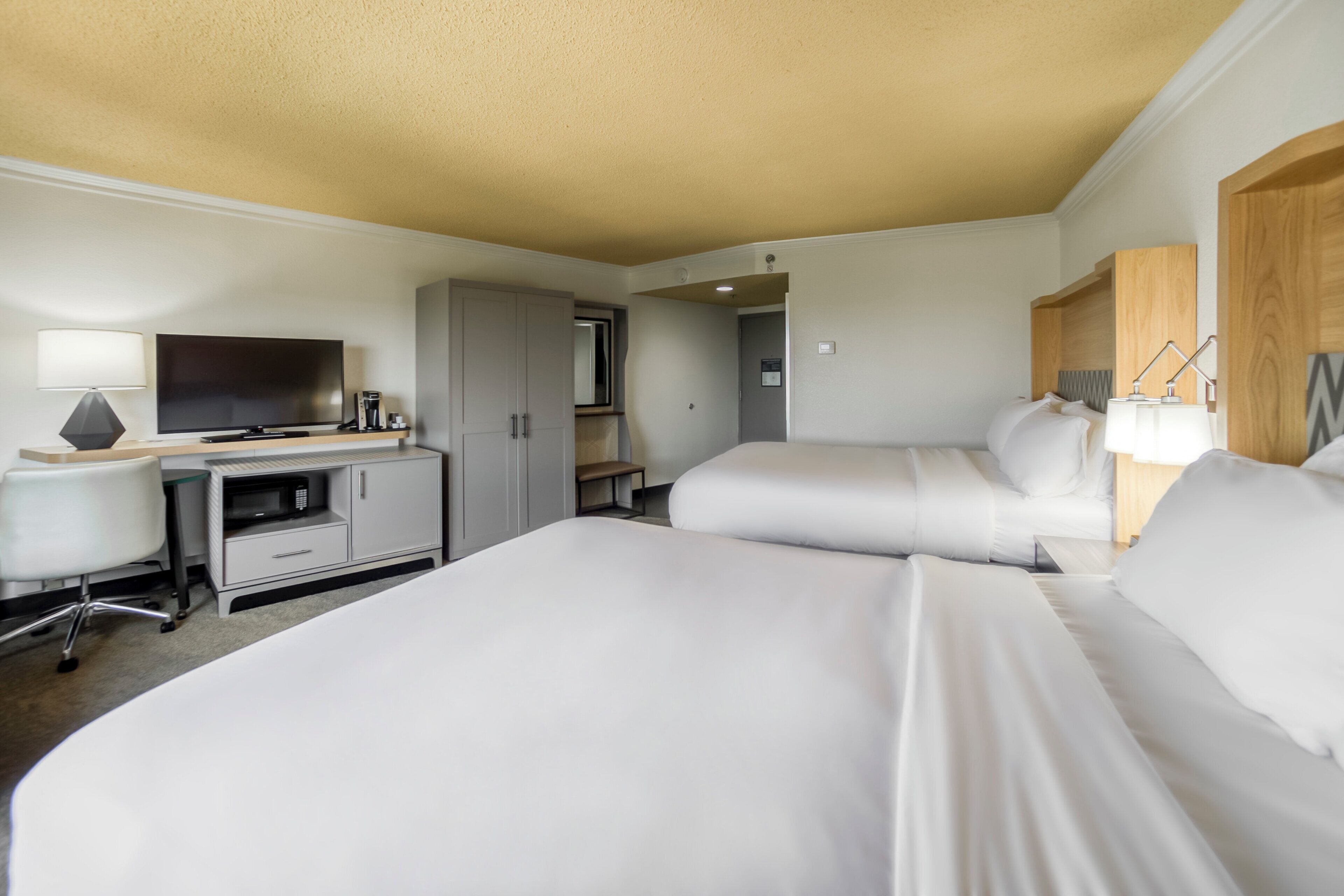 A hotel room with two beds, a desk with a TV, a chair, and a wardrobe.