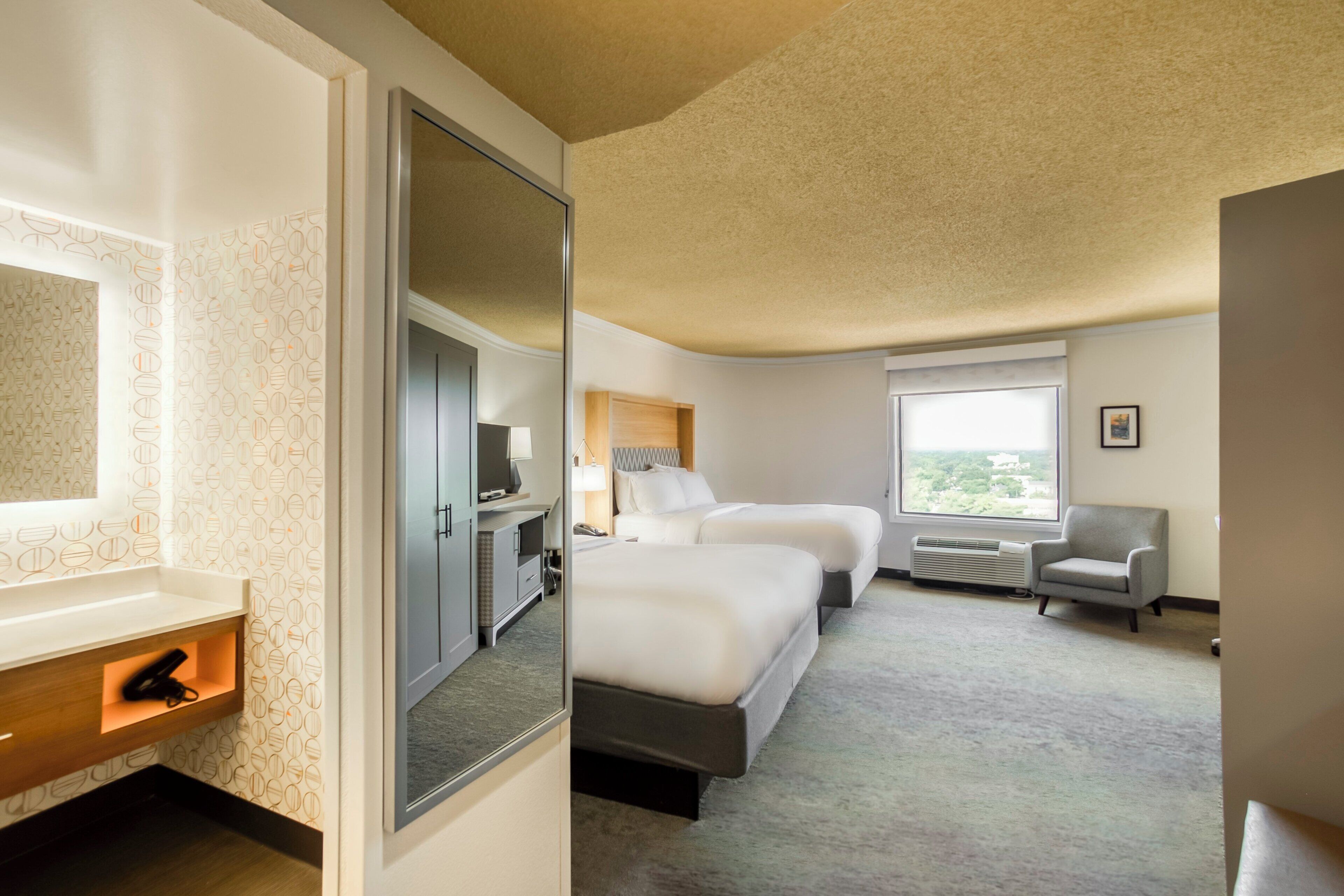 A hotel room with a bed, a desk, a chair, and a window.