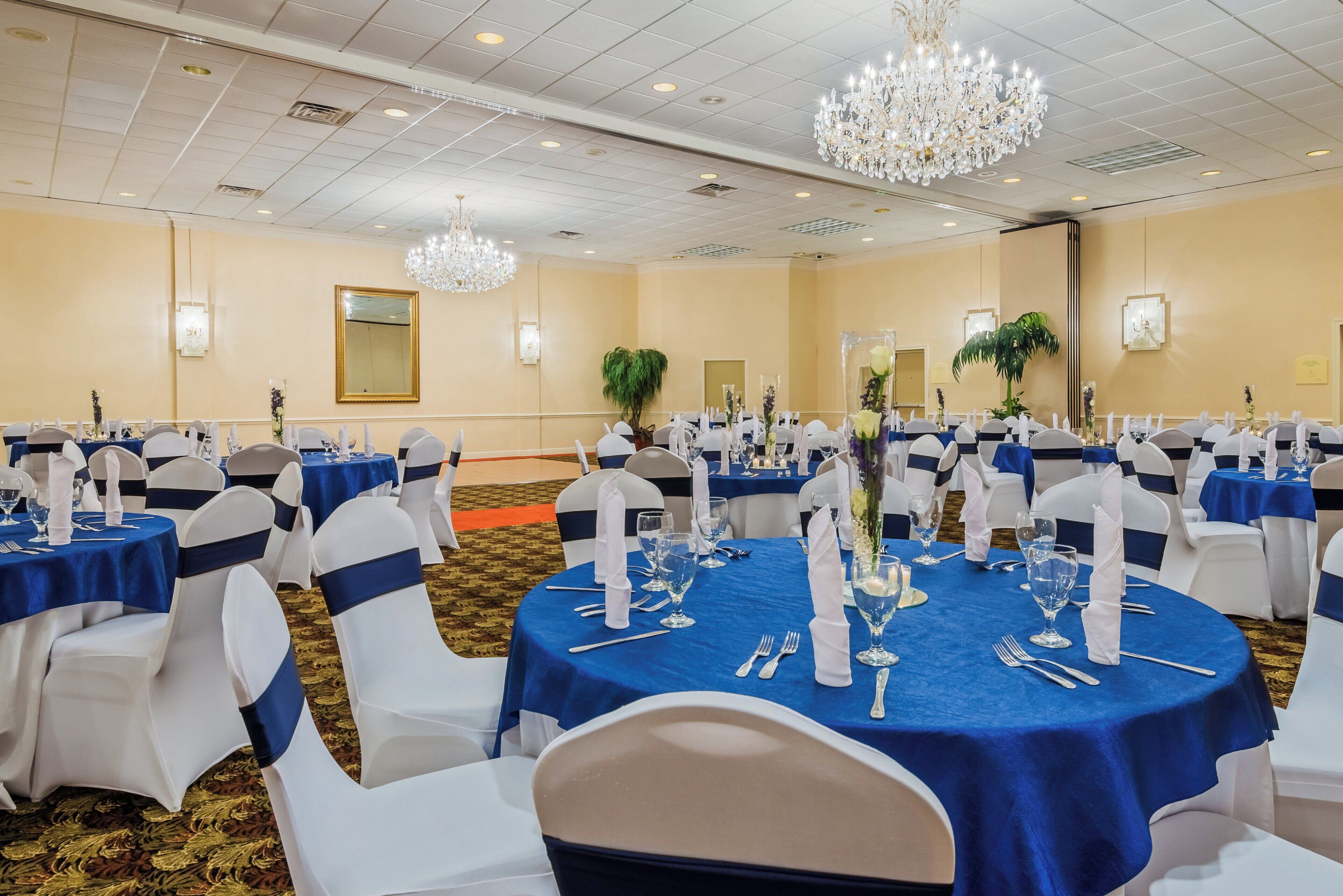 A banquet hall with round tables, white chairs, and blue tablecloths.