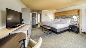 A hotel room with a bed, bedside table, lamp, TV, desk, chair, and a bench. - Holiday Inn Mobile-Dwtn/Hist. District by IHG (Mobile)