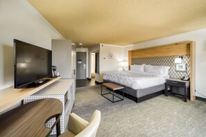 A hotel room with a bed, bedside table, lamp, TV, desk, chair, and a bench. - Holiday Inn Mobile-Dwtn/Hist. District by IHG (Mobile)