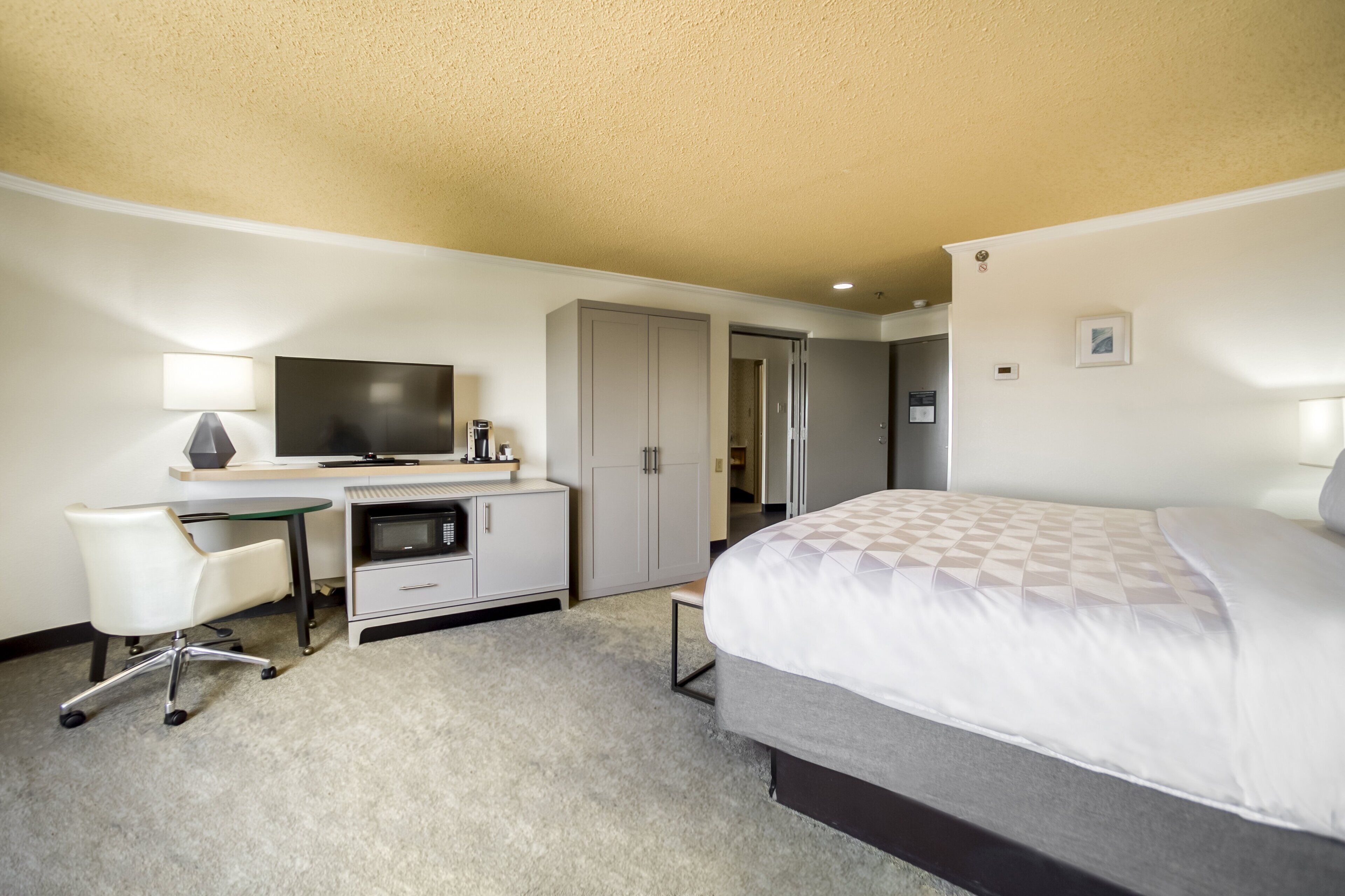 A hotel room with a bed, a desk with a computer, a chair, a television, and a wardrobe.