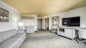 A compact living space with a grey sofa, a flat-screen TV, a small kitchenette, and a dining area. - Holiday Inn Mobile-Dwtn/Hist. District by IHG (Mobile)