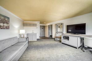 A compact living space with a grey sofa, a flat-screen TV, a small kitchenette, and a dining area. - Holiday Inn Mobile-Dwtn/Hist. District by IHG (Mobile)