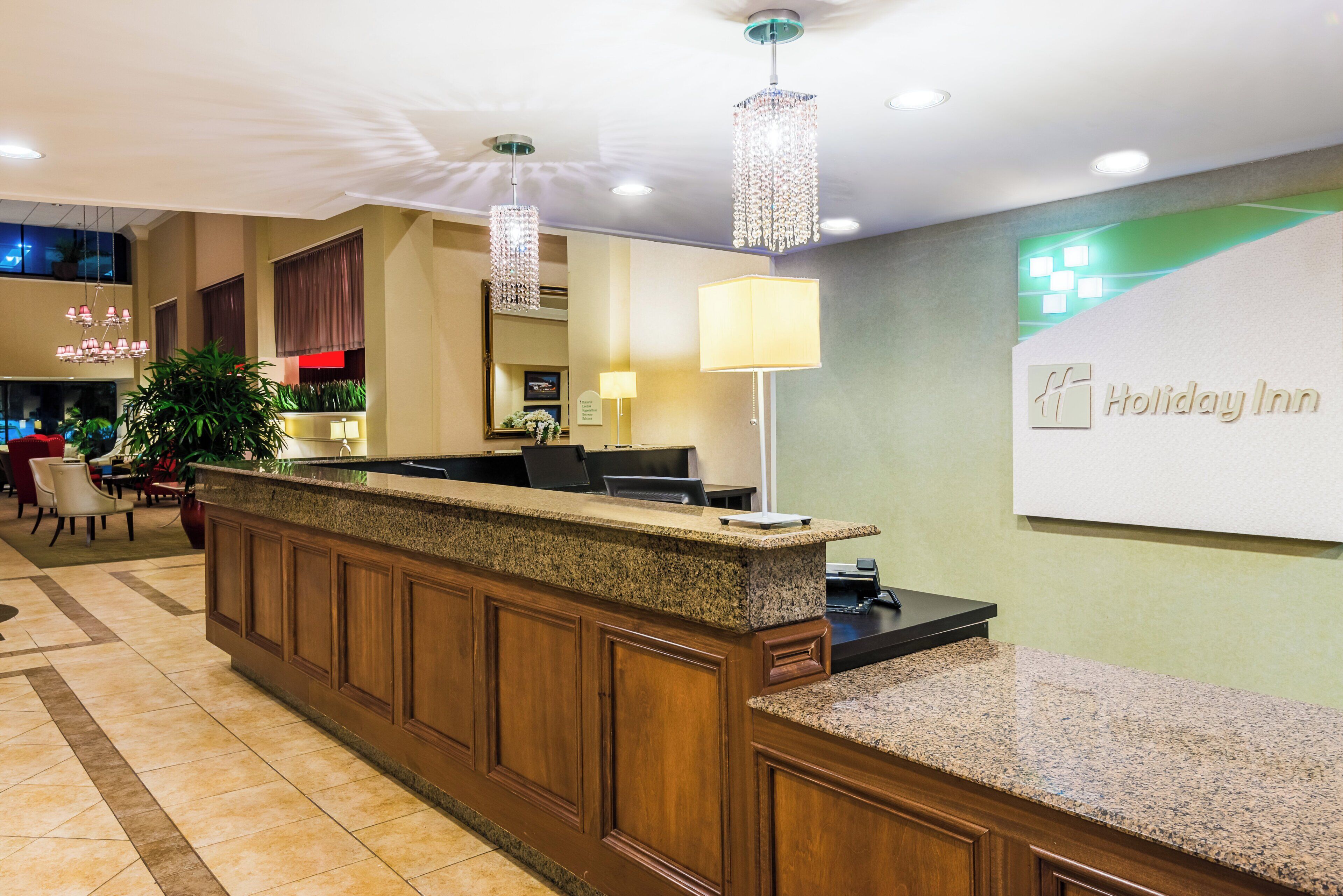A hotel reception area with a reception desk, a chandelier, and a wall sign for the Holiday Inn.