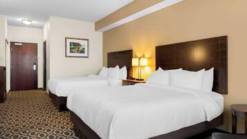 A hotel room with two beds, a nightstand with a lamp, a framed picture on the wall, and a patterned carpet.