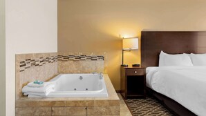 A hotel room with a large bathtub, a bed with white linens, a nightstand, and a wall-mounted lamp. - Best Western Paradise Inn (Savoy)