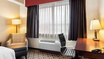 Een hotelkamer met een bed, een bureau, een stoel, een verwarming en een raam met gordijnen.
