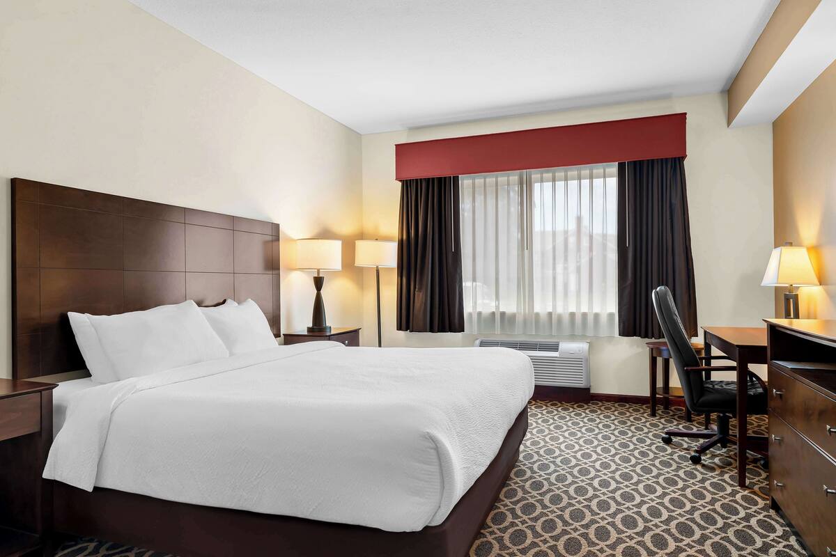 Habitación de hotel con una cama grande, dos mesitas de noche con lámparas, un escritorio con silla y una ventana con cortinas.