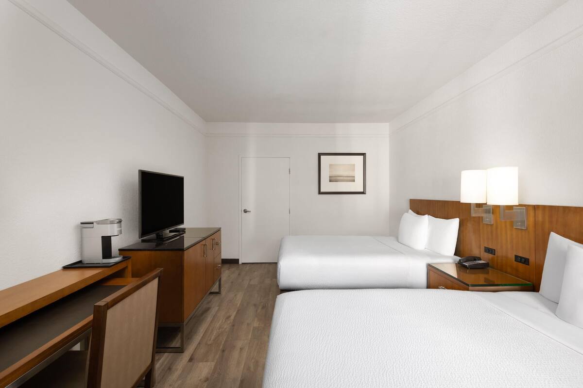 Een hotelkamer met twee bedden, een bureau met koffiezetapparaat, een televisie en een nachtkastje met lampen.