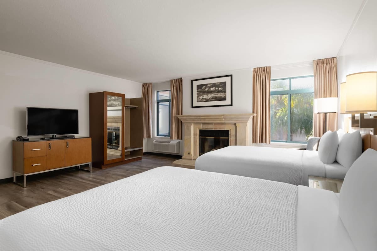 Een hotelkamer met twee bedden, een televisie, een kledingkast, een open haard en een raam met gordijnen.
