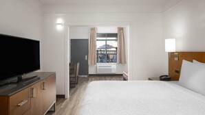 Ein Hotelzimmer mit einem großen Bett, einem Fernseher auf einer Holzkassette, einem Schreibtisch mit Stuhl und einem fenster mit Vorhängen.