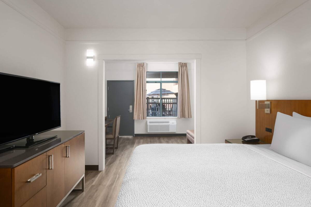 Hotelkamer met een groot bed, een televisie op een houten kast, een bureau met stoel, en een raam met gordijnen.