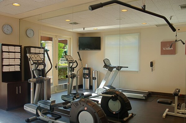 A gym with cardio machines, a TV, and a mirror.