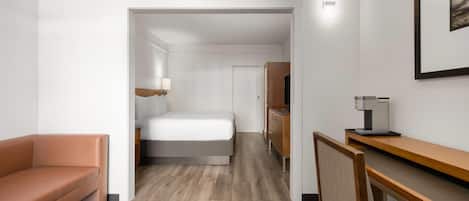 A hotel room with a bed, a desk, a chair, a sofa, and a TV.