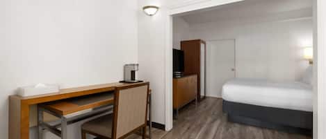 Una habitación de hotel con un escritorio de madera, una silla, una cama, un televisor y un armario.