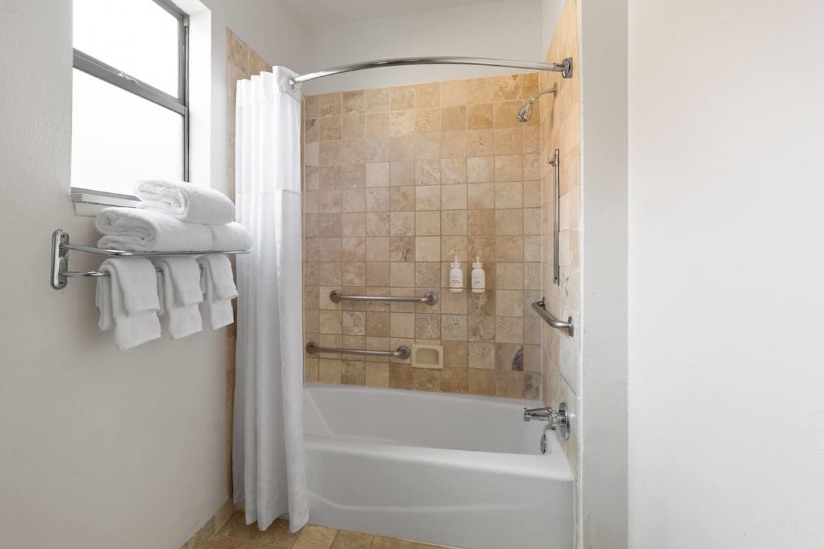 Een badkamer met een bad, douche en een raam. Handdoeken liggen op een rek en er hangt een douchegordijn.