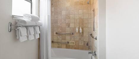 Un baño con bañera, ducha y ventana. Hay toallas en un perchero y una cortina de ducha.