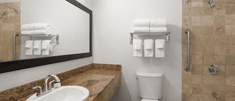 Un baño moderno con lavamanos de granito, inodoro blanco, cabina de ducha de vidrio y toallero.