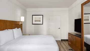 Habitación de hotel con una cama grande, cabecera de madera, mesita de noche con lámpara, televisor y un cuadro en la pared.