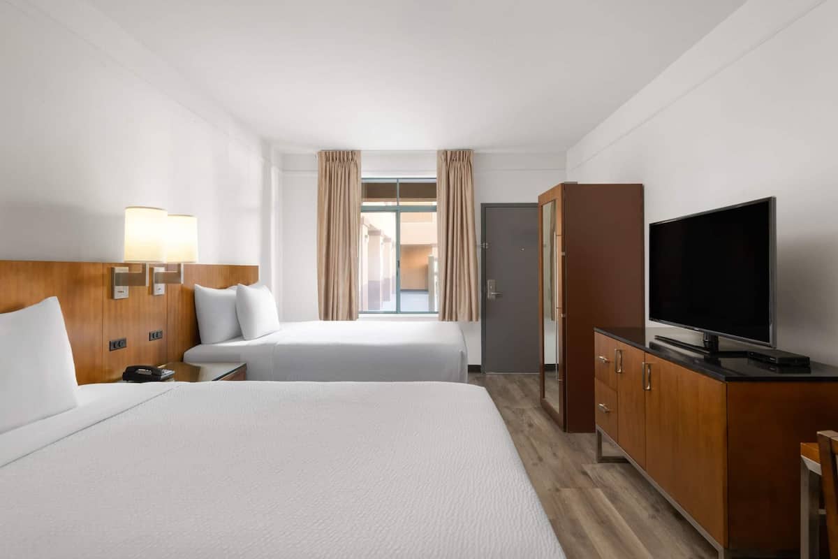 Een hotelkamer met twee bedden, een televisie, houten meubels en een raam met gordijnen.