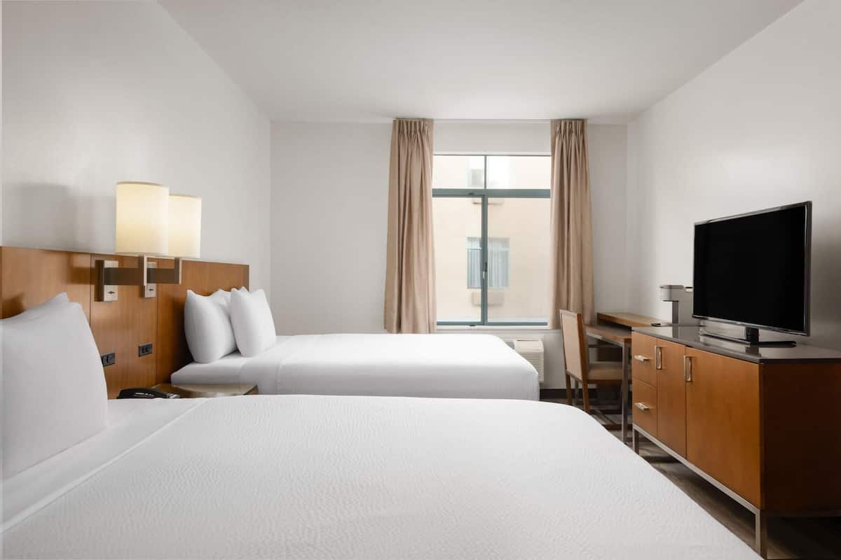 Een hotelkamer met twee bedden, een bureau, een televisie en een raam met gordijnen.