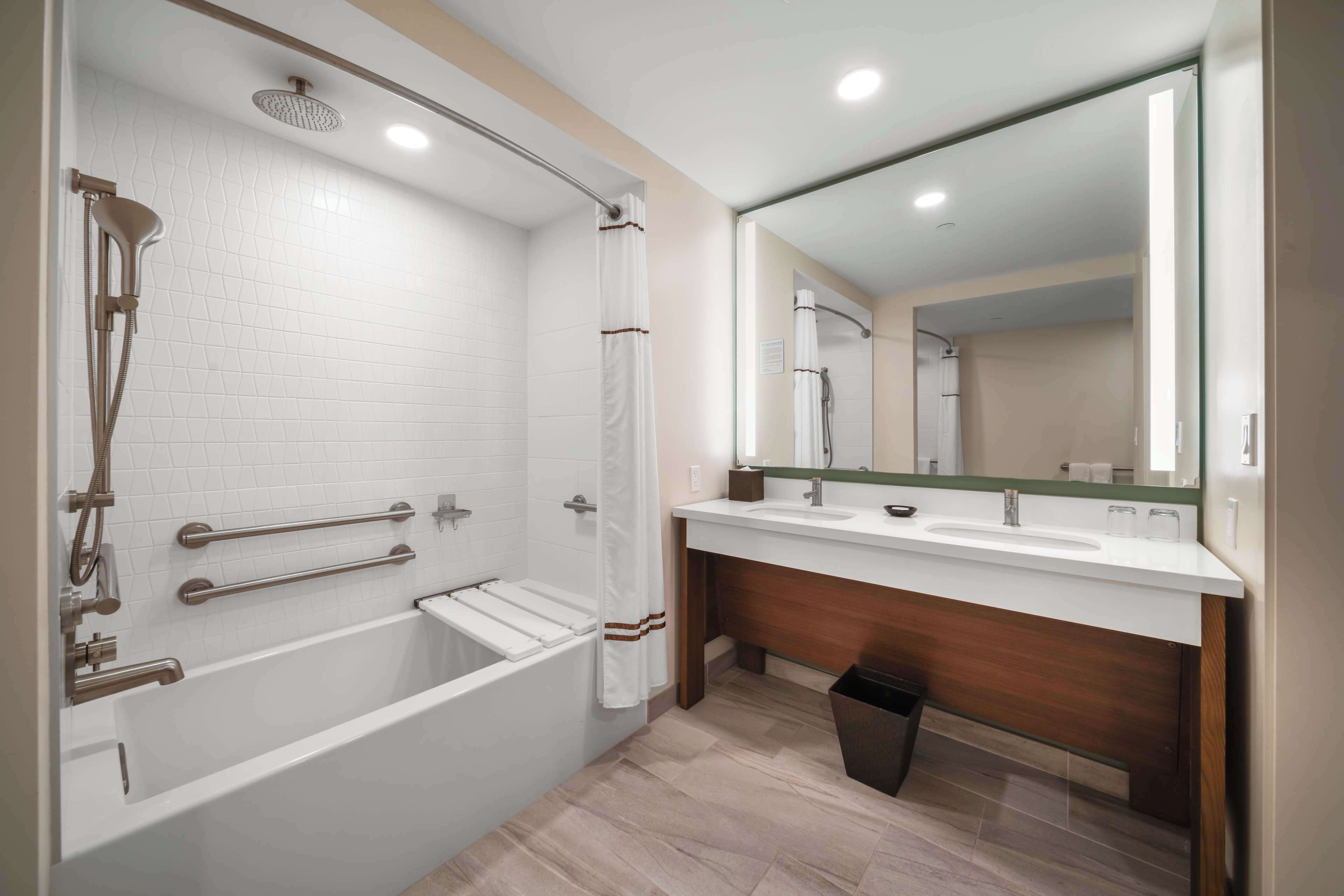 Une salle de bain moderne équipée d’une baignoire, d’une douche, d’un meuble-lavabo avec miroir et d’une poubelle.