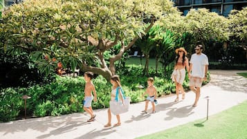 A pathway with a group of people walking, surrounded by greenery and a building in the background.