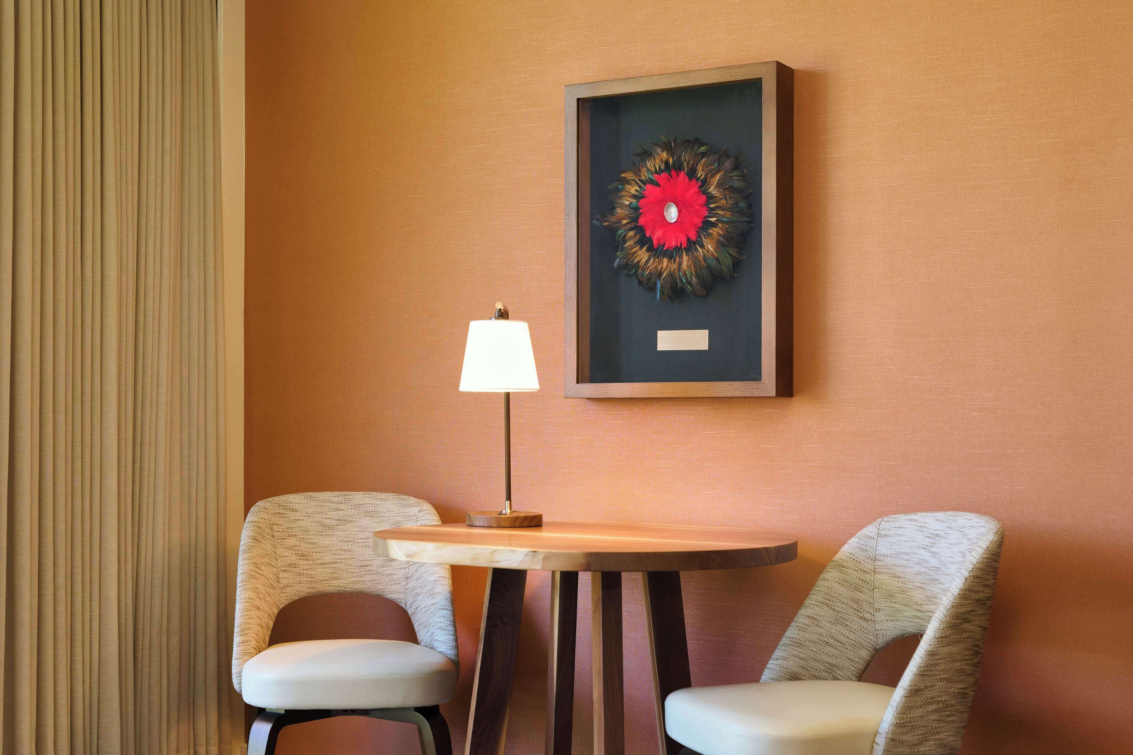 Een kamer met twee stoelen, een tafel, een lamp en een lijst met een kunstwerk aan de muur.