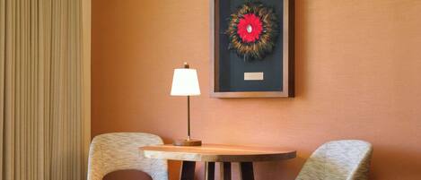Een kamer met twee stoelen, een tafel, een lamp en een lijst met een kunstwerk aan de muur.