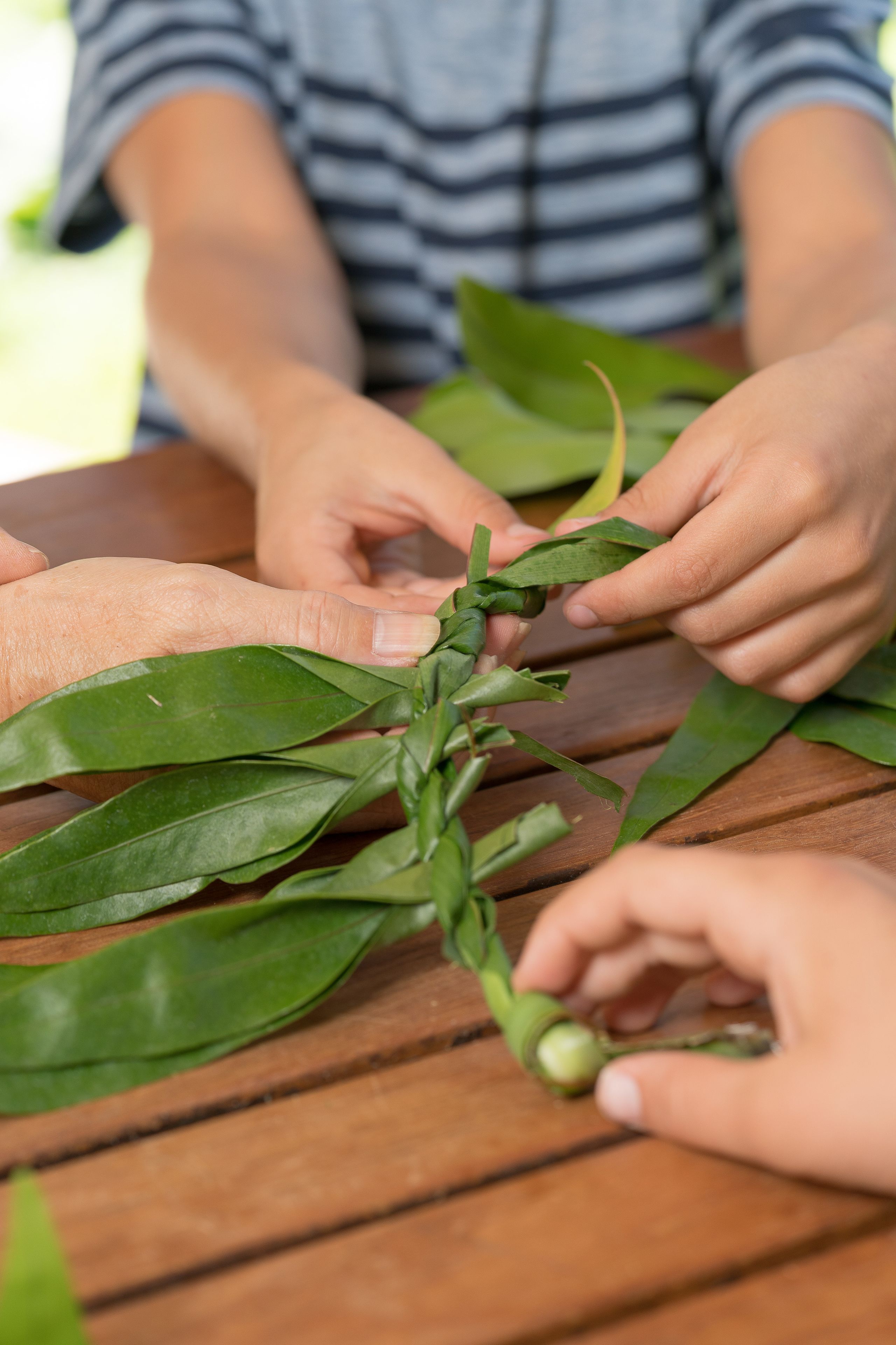 A person braiding green leaves on a wooden table.