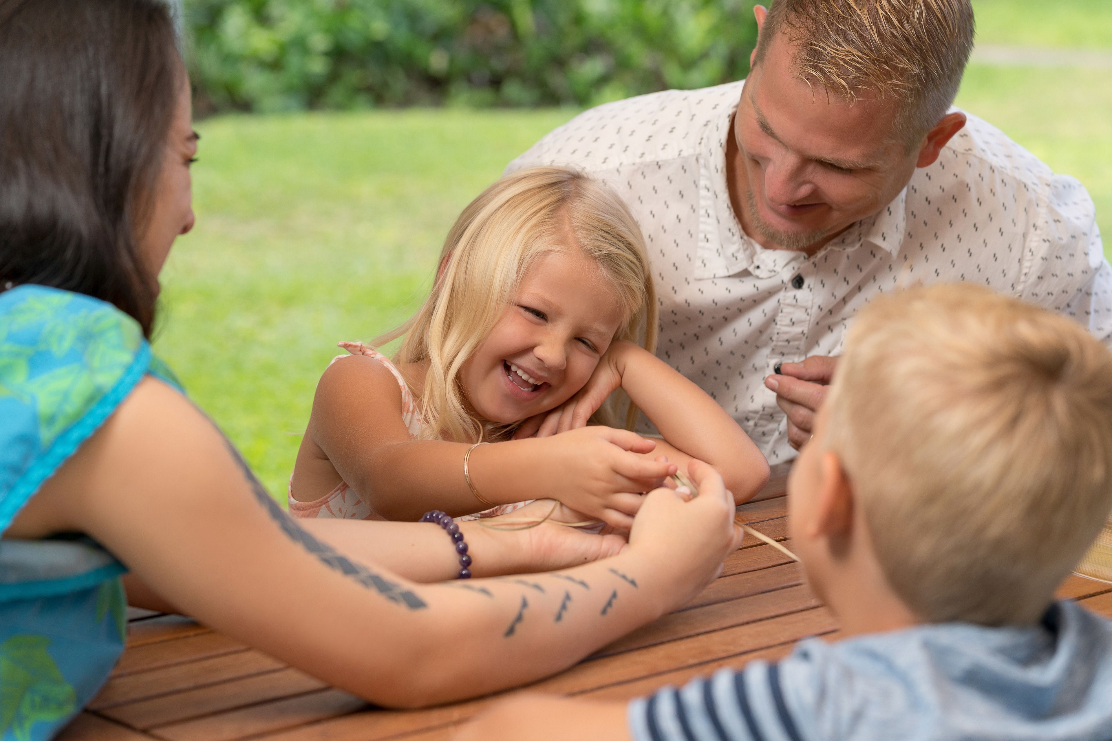 A family of four seated at a wooden table outdoors.