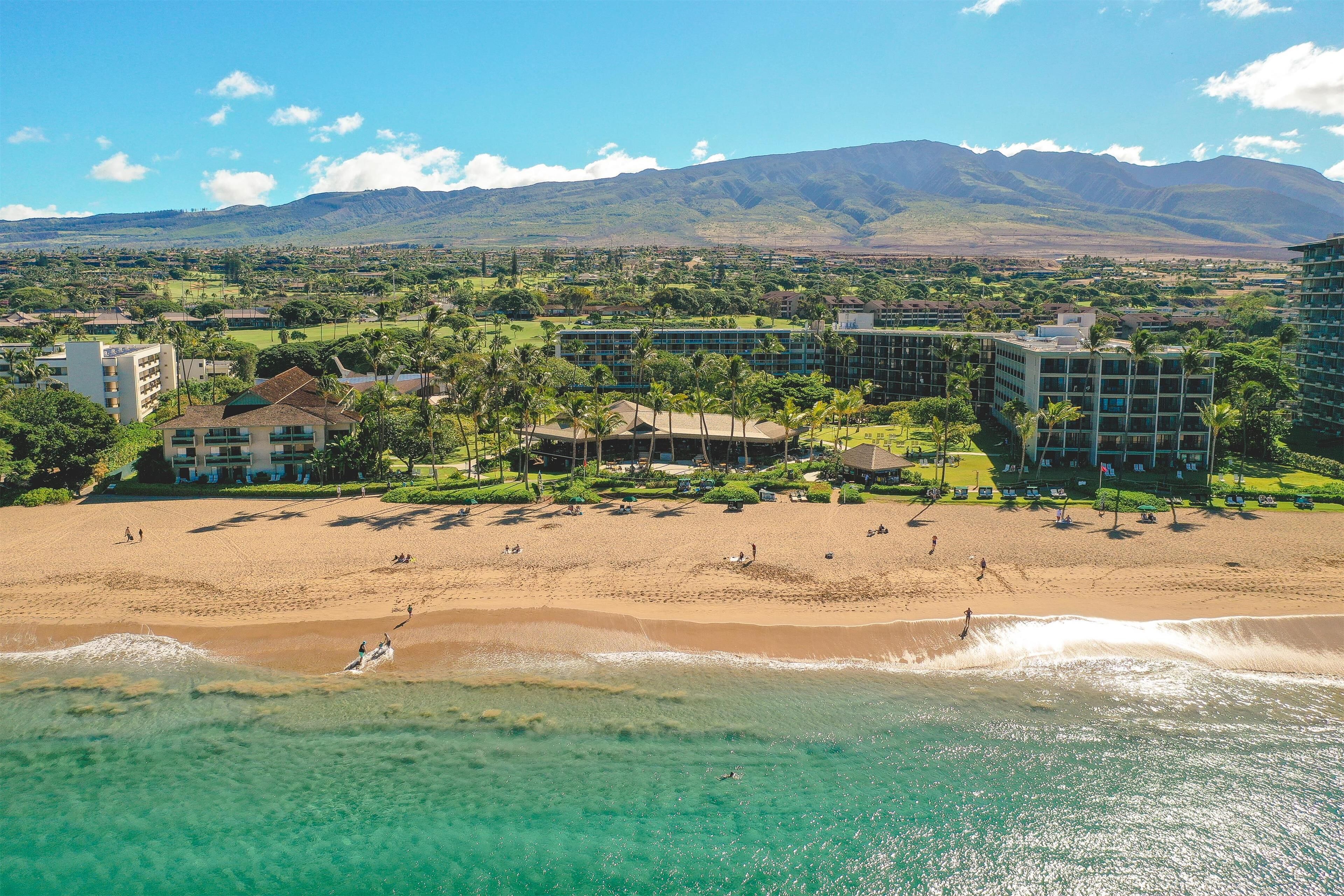 A beach resort with multiple buildings, a sandy beach, and a mountain in the background.
