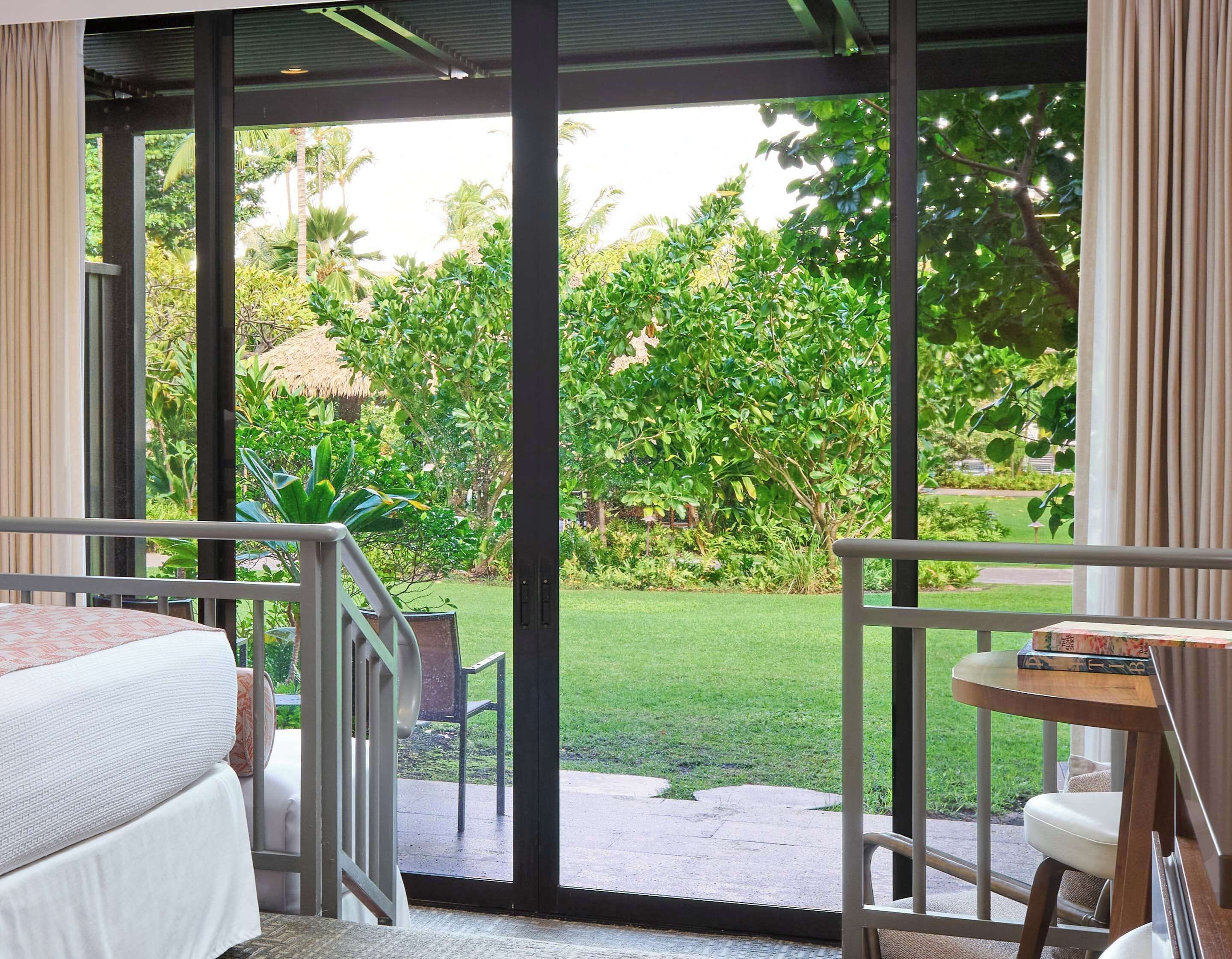 Una habitación con cama, una mesita, una silla y un balcón con vistas a un jardín.