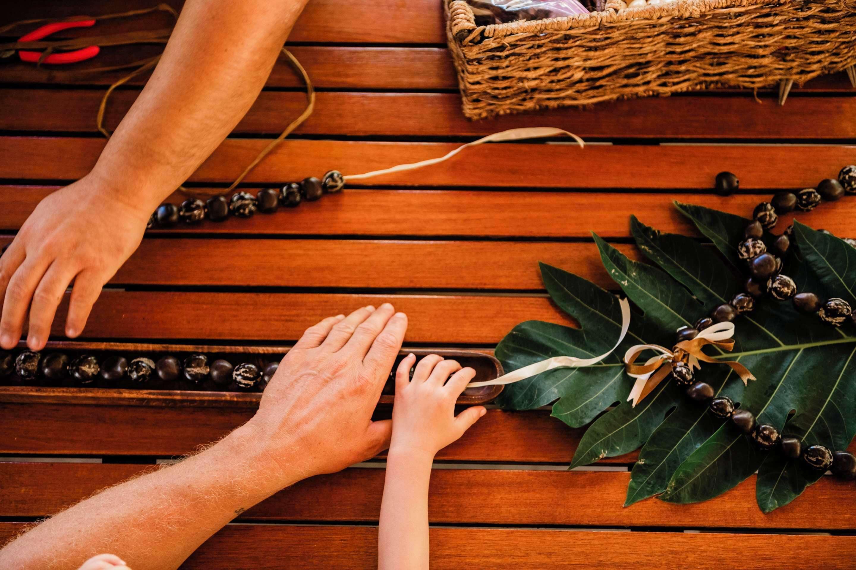Une table en bois sur laquelle des mains disposent des perles et une feuille.