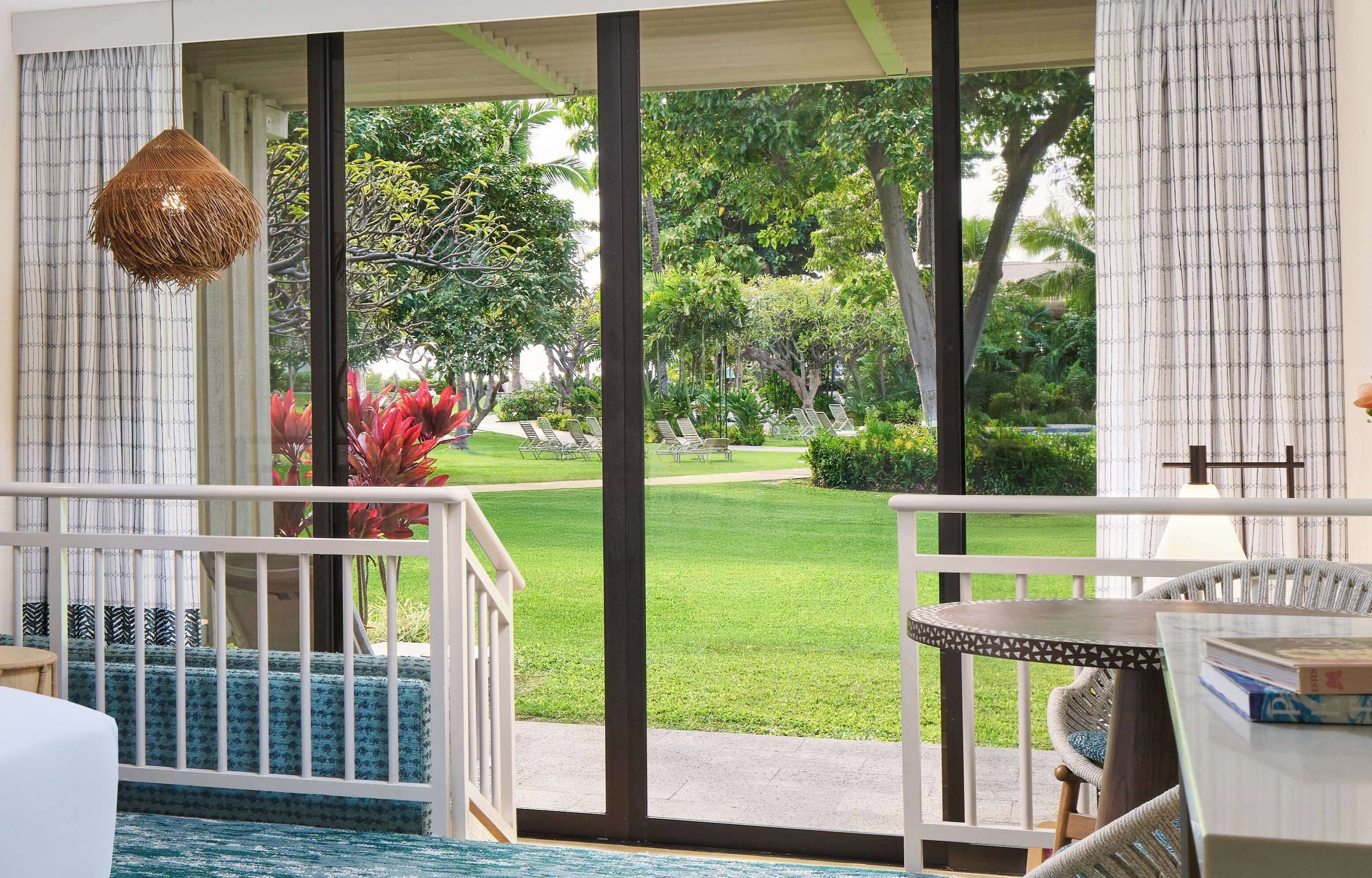 A room with a large sliding glass door, a wicker chair, a small table, and a hanging light fixture.