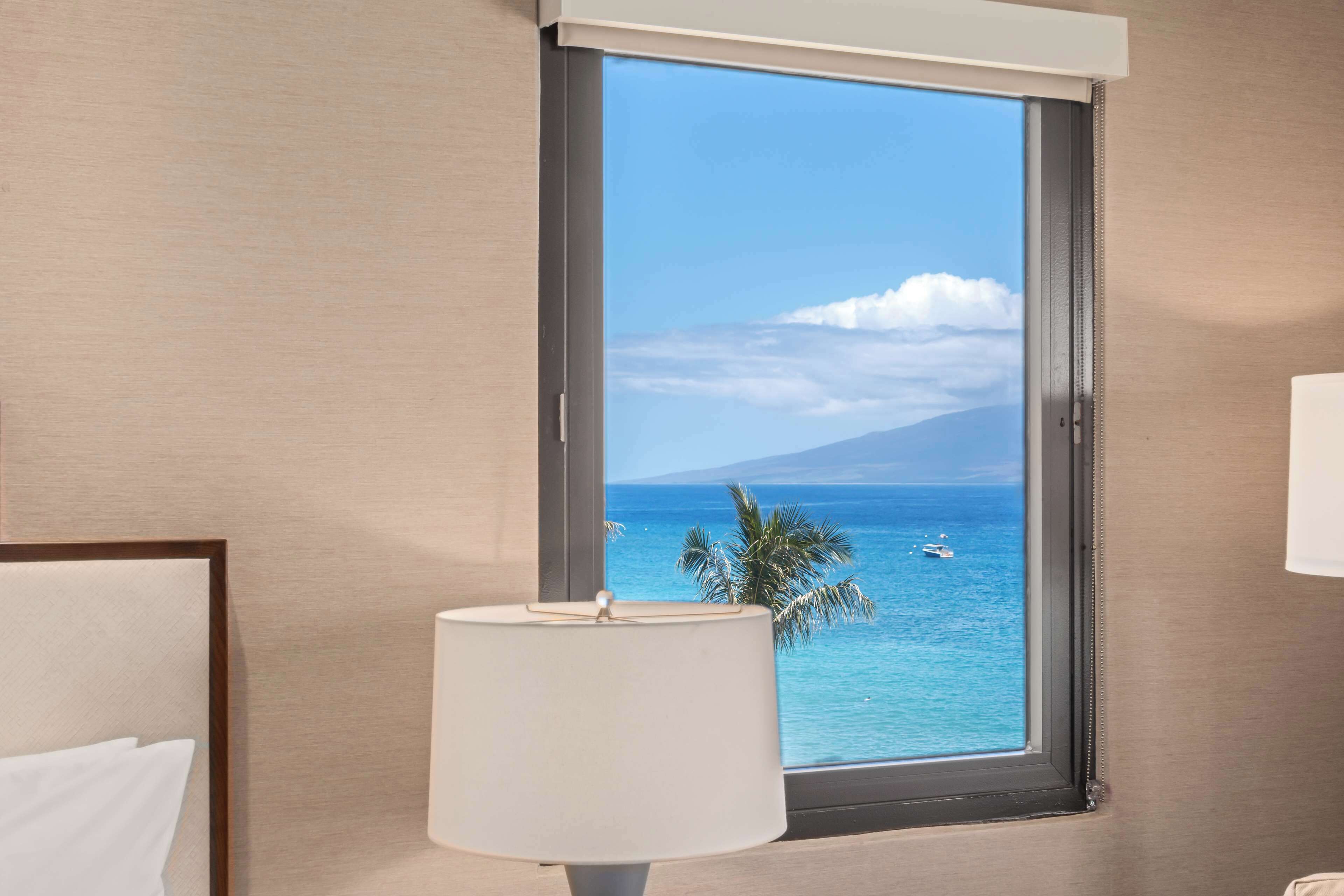 Habitación de hotel con un ventanal amplio que ofrece vistas al océano y a la montaña.