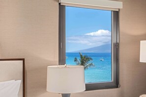 A hotel room with a large window offering a view of the ocean and a mountain.
