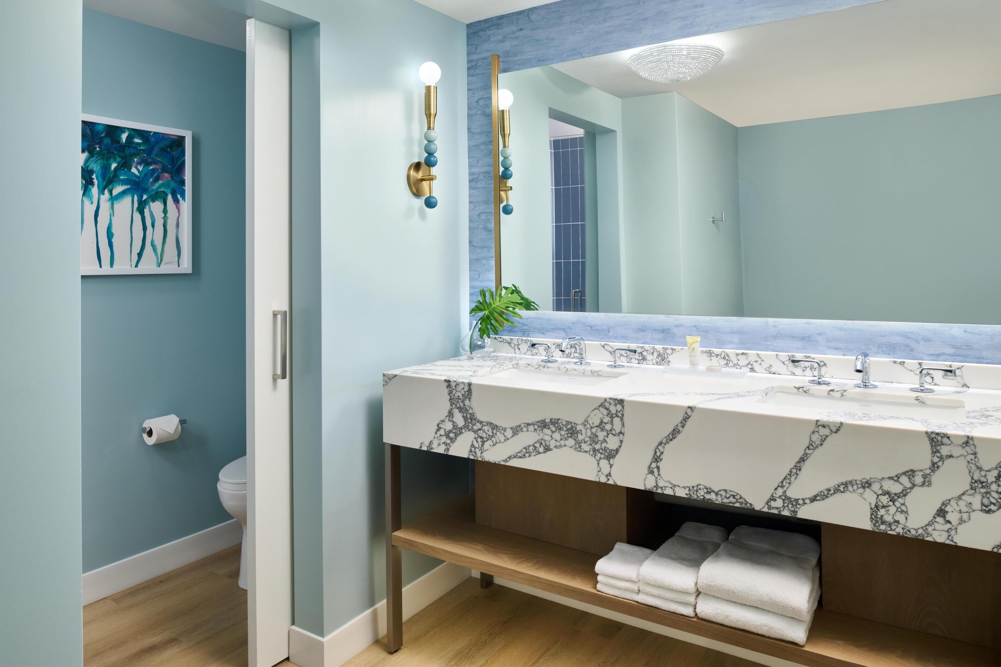 Ein Badezimmer mit Marmorwaschtisch, einem großen Spiegel und einer Toilette.