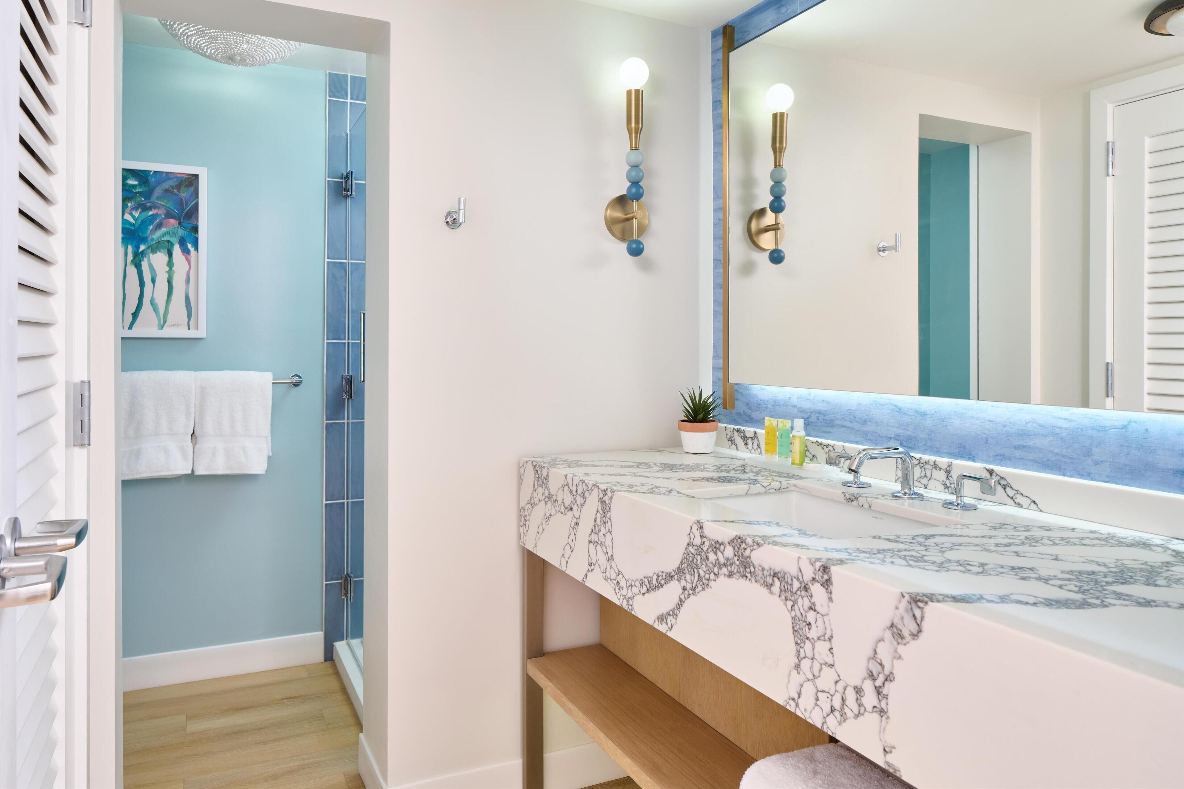 A bathroom with a marble sink, a large mirror, and a blue shower enclosure.