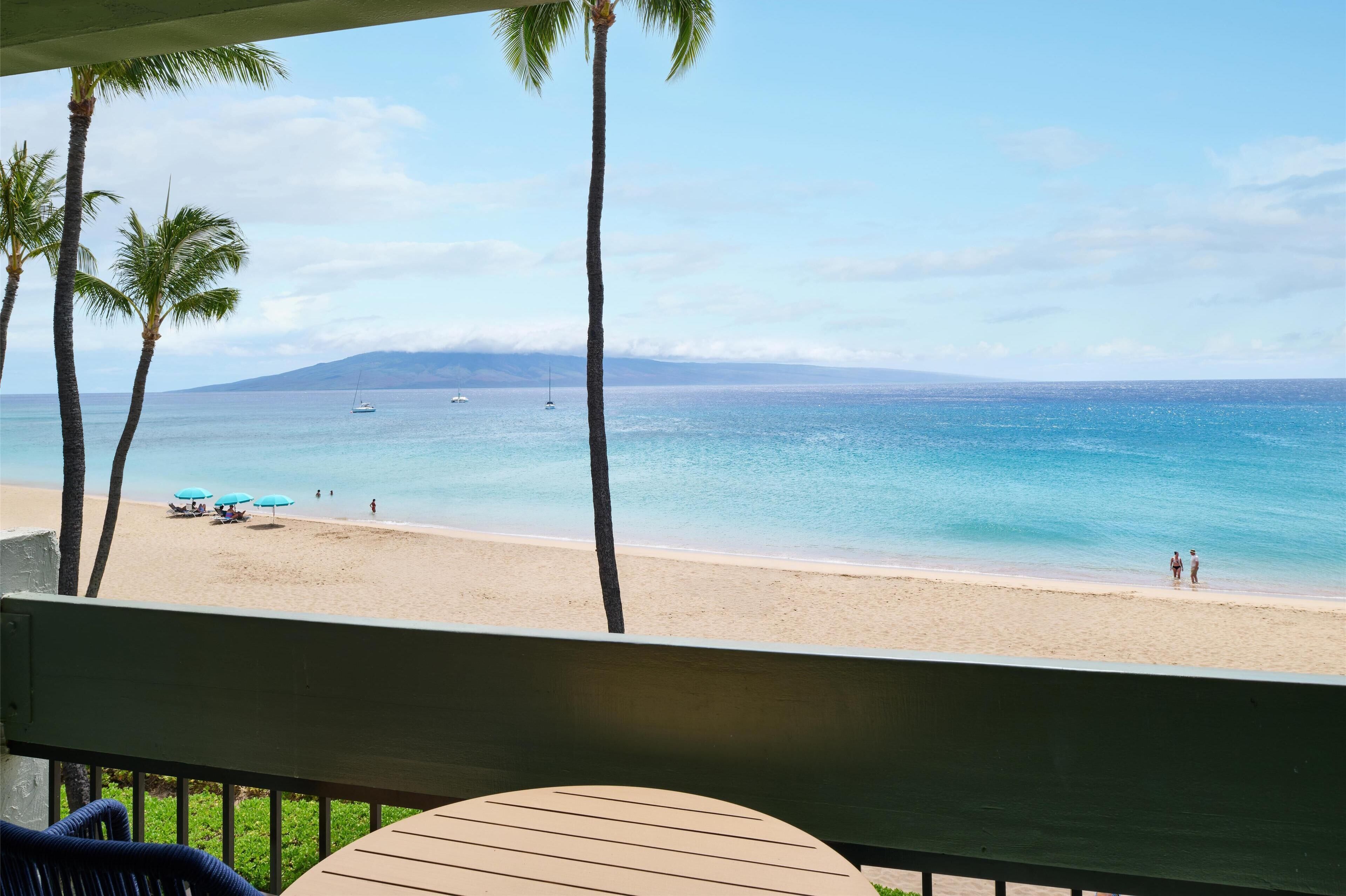 A beach view with palm trees, a sandy beach, and a few boats in the water.