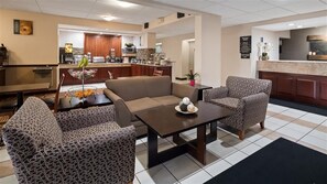 A hotel lobby with a reception desk, a sofa, patterned chairs, and a dining area with a buffet. - Baymont by Wyndham Monroe Ohio (Monroe)