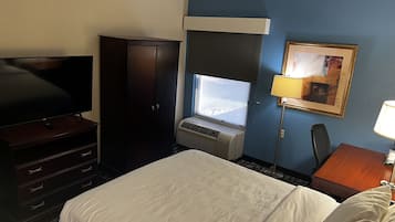 Habitación de hotel con cama, televisión, armario, escritorio con lámpara y ventana con vistas.
